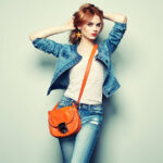 Fashion portrait of beautiful young woman with red hair. Girl in blouse and jeans. Jewelry and hairstyle. Girl with handbag